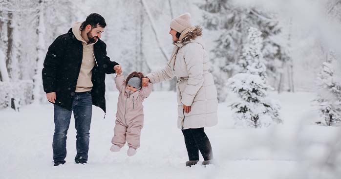 Couple holding toddler's hands while outside in a snowy forest.