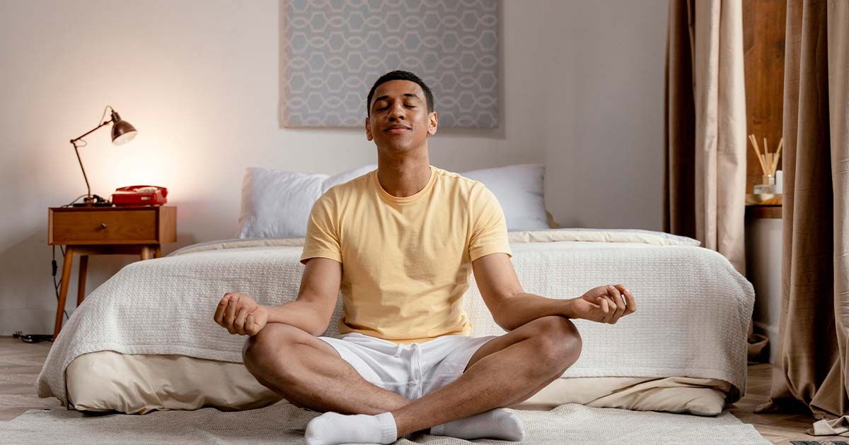Man sitting on bedroom floor while meditating.
