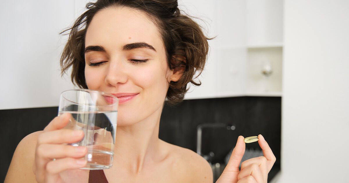 Woman smiling with a supplement in her  hand, drinking water.