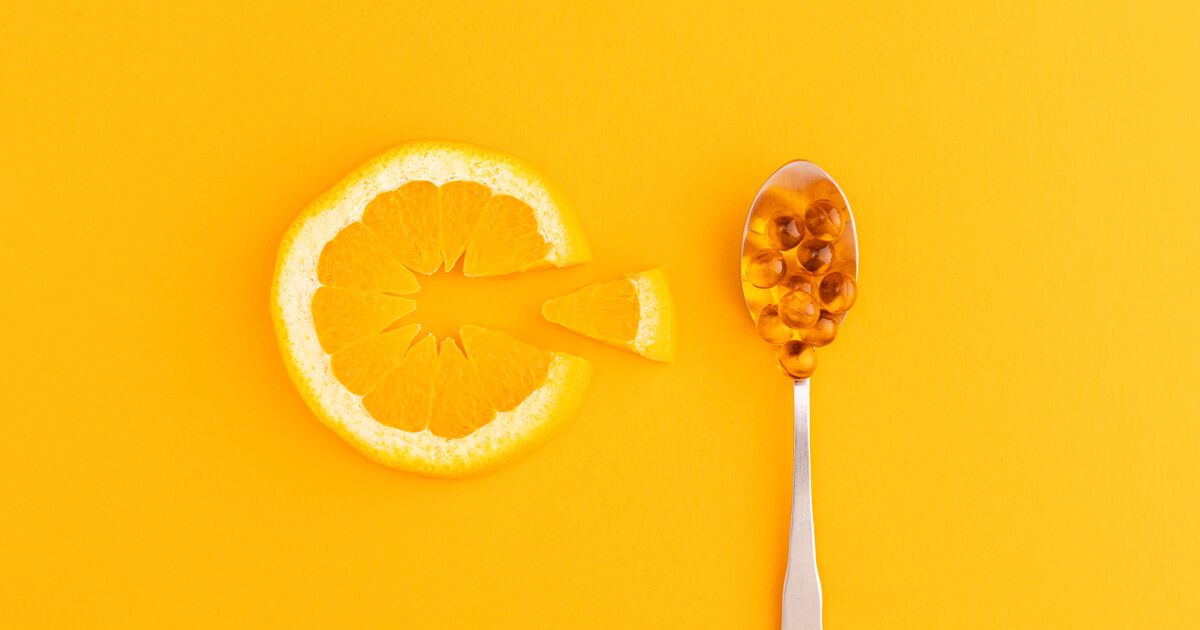 Orange slice in the shape of a 'C' with a spoon full of vitamin c supplements beside it.
