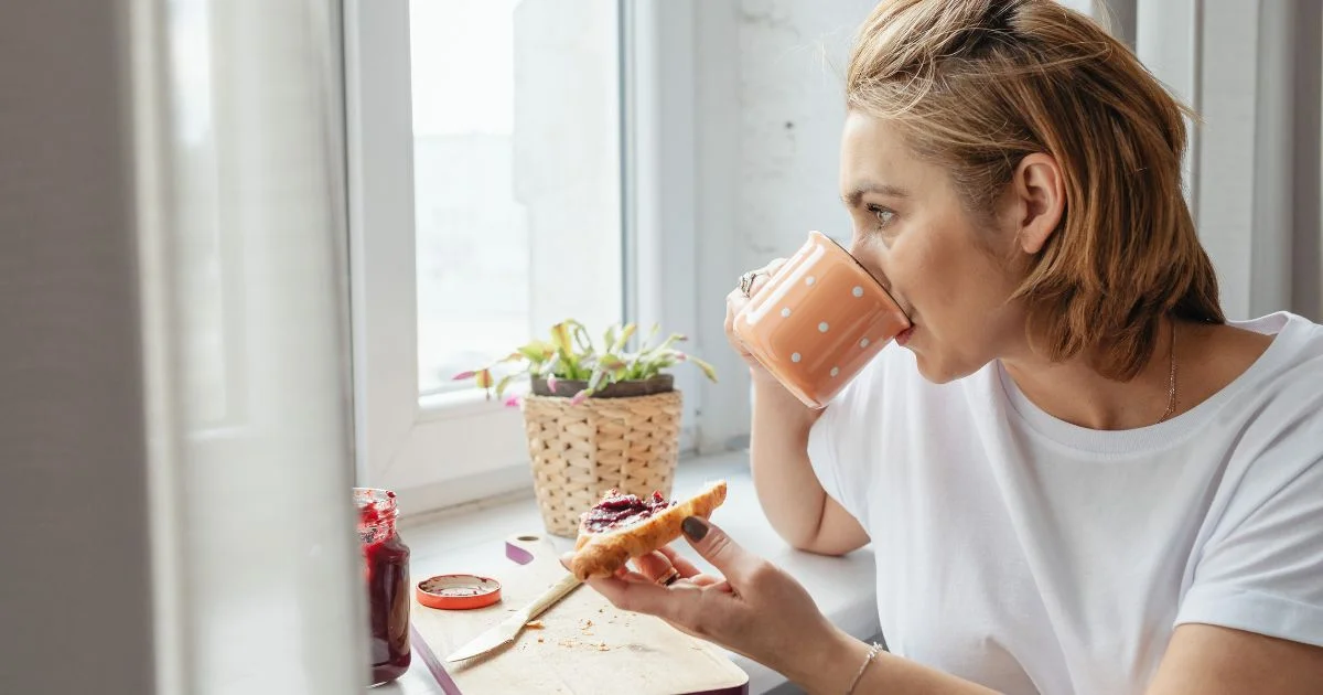 Woman drinking coffee and eating toast by a window