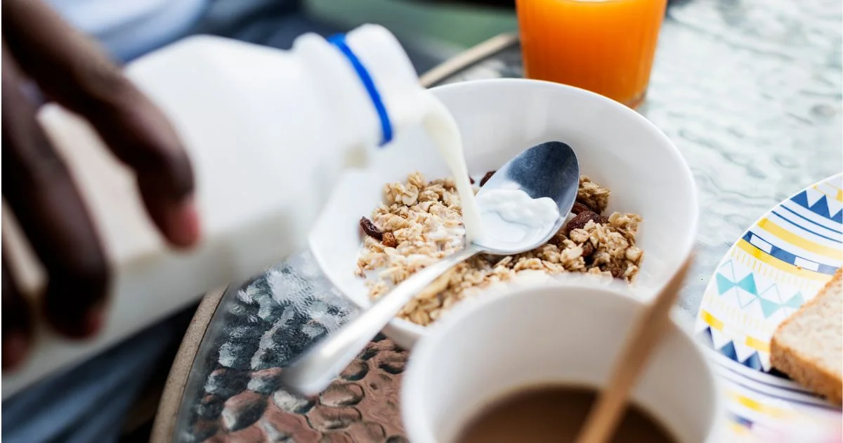 Milk poured over granola beside coffee, juice and toast